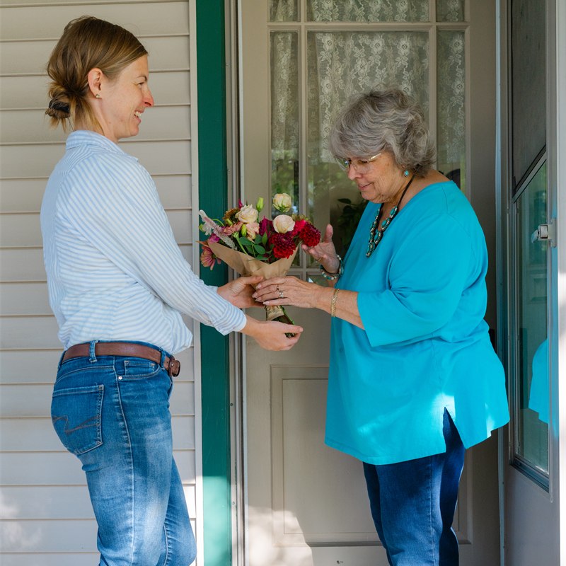 Anna handing a wrapped flower subscription bouquet to a smiling mom at her front door